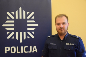 dzielnicowy Huras przy banerze z napisem policja