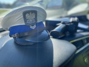na zdjęciu policyjna biała czapka na desce rozdzielczej w samochodzie, przy której leży policyjny miernik prędkości