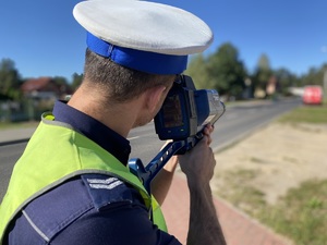 na zdjęciu policjant z miernikiem prędkości przy drodze