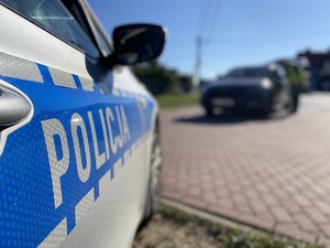 na zdjęciu fragment radiowozu z napisem policja, przed nim inny czarny pojazd