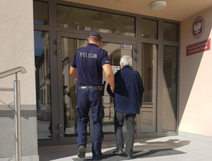 na zdjęciu policjant prowadzi zatrzymanego do budynku prokuratury