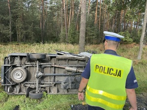 na zdjęciu policjant przed dostawczym samochodem, który leży w rowie