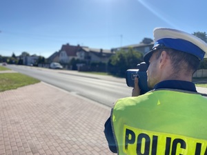 na zdjęciu policjant przy drodze sprawdzający radarem prędkość pojazdów