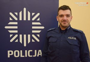 na zdjęciu dzielnicowy Łazaj przy banerze z napisem policja