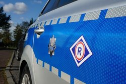 na zdjęciu logo ruchu drogowego na niebieskim tle, na drzwiach radiowozu