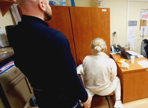 na zdjęciu policjant przy zatrzymanej kobiecie, która siedzi na krześle