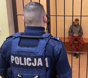 na zdjęciu policjant obserwuje w celi zatrzymanego mężczyznę