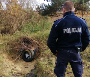 na zdjęciu policjant a przed nim wykopany dół, w którym znajdują się skradzione butelki przykryte krzakami