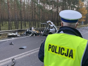 na zdjęciu policjant w kamizelce odblaskowej stojący przed rozbitym samochodem osobowym koloru srebrnego przy drogowych barierkach