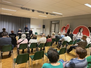 na zdjęciu osoby na krzesłach, przed nimi policjanci przy stoliku