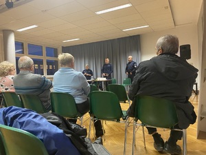 na zdjęciu osoby na krzesłach, przed nimi policjanci