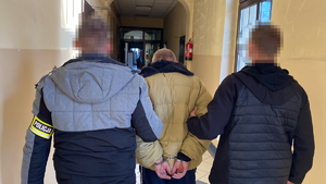 na zdjęciu policjanci prowadzą zatrzymanego korytarzem komendy