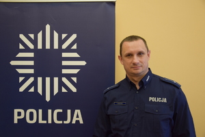 policjant w niebieskim mundurze, obok niebieski baner z napisem policja