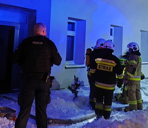 na zdjęciu policjant i strażacy przed budynkiem