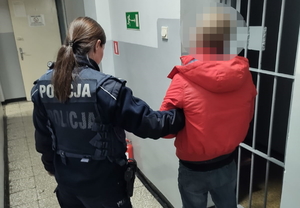 na zdjęciu policjantka trzyma za rękę złodzieja w korytarzu komisariatu