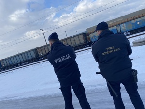 na zdjęciu policjant i strażnik ochrony kolei a przed nimi wagony pociągu