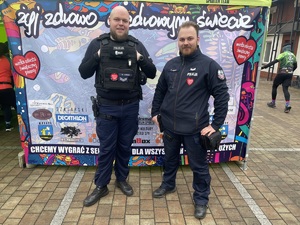 na zdjęciu dwóch policjantów stojących przed banerem reklamującym wielką orkiestrę świątecznej pomocy