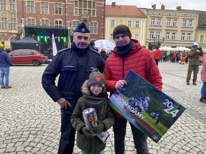 na zdjęciu policjant i mężczyzna z dzieckiem, który trzyma w ręku kalendarz policyjny, za nimi ratusz i płyta rynku
