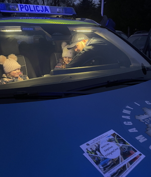 na zdjęciu dzieci w radiowozie i policjant schylający się przez otwarte drzwi kierowcy