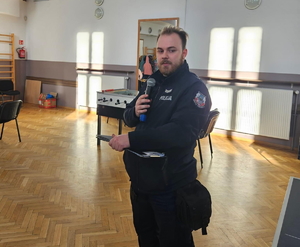 na zdjęciu dzielnicowy z mikrofonem w ręku w sali