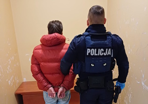 na zdjęciu policjant trzyma zatrzymanego za ramię