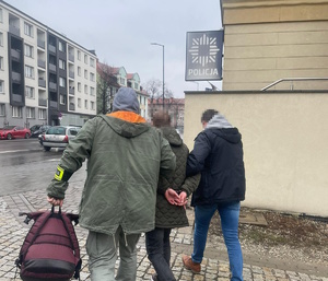 na zdjęciu policjanci po cywilu prowadzą zatrzymanego do komendy
