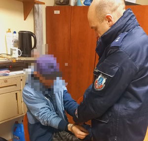 na zdjęciu policjant stoi przed zatrzymanym, który siedzi na krześle