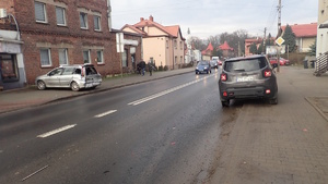 na zdjęciu droga, na chodniku po lewej i po prawej uszkodzone samochody, na chodniku osoby, na jezdni inne pojazdy