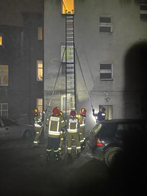 na zdjęciu policjanci i strażacy przy drabinie opartej o budynek w trakcie ewakuacji mieszkańców kamienicy