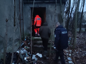 na zdjęciu policjant, ratownik i pracownik socjalny w trakcie wejścia do pustostanu