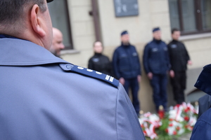 na zdjęciu fragment policyjnego munduru a w oddali warta honorowa pod tablicą