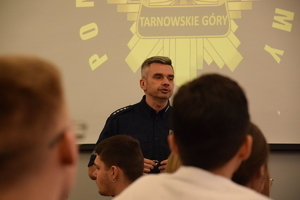 na zdjęciu policjant mówiący do uczniów, za nim na ścianie wyświetlana gwiazda policyjna z napisem tarnowskie góry