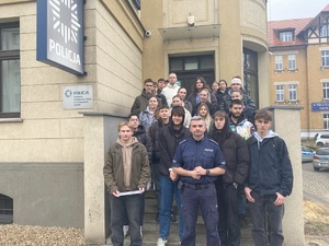 grupowe zdjęcie uczniów i policjanta na schodach wejściowych do budynku komendy