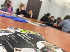 na zdjęciu ulotka informacyjna z napisem zostań śląskim policjantem, z tyłu widoczni uczniowie siedzący w ławkach