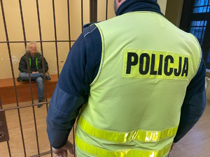 na zdjęciu w celi mężczyzna, przed celą policjant