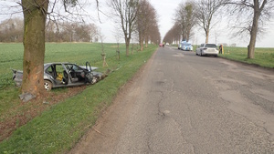 na zdjęciu fragment drogi, po lewej rozbity pojazd przy drzewie, po prawej radiowozy i srebrny samochód