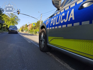na zdjęciu fragment radiowozu a przed nim inny pojazd na jezdni