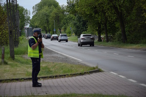 na zdjęciu policjant przy drodze kontrolujący prędkość pojazdów