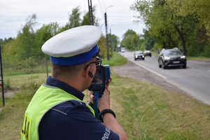 na zdjęciu policjant przy drodze kontrolujący prędkość pojazdów