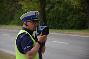 na zdjęciu policjant przy drodze kontrolujący prędkość pojazdów