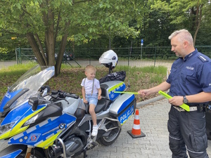 na zdjęciu dziecko na policyjnym motocyklu, obok niego policjant wręczający odblask