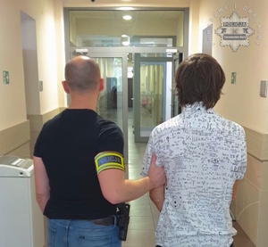 na zdjęciu policjant prowadzi zatrzymanego korytarzem