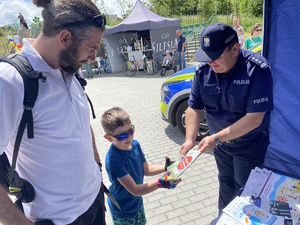 na zdjęciu komendant policji wręczający dziecku kolorowankę, obok mężczyzna