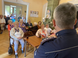 na zdjęciu policjant a przed nim na krzesłach uczestnicy debaty