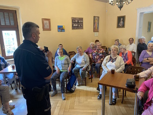 na zdjęciu policjant a przed nim na krzesłach uczestnicy debaty