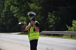 na zdjęciu policjant przy jezdni z miernikiem prędkości