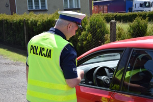na zdjęciu policjant przy czerwonym samochodzie w trakcie kontroli