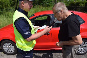 na zdjęciu policjant bada trzeźwość mężczyzny przy czerwonym samochodzie