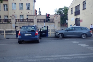 na zdjęciu dwa pojazdy, jeden niebieski tyłem do aparatu, w poprzek drogi, drugo obok niego wbity w barierkę chodnikową