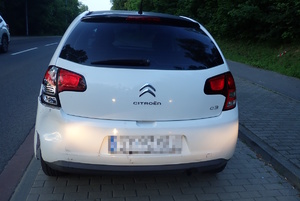 na zdjęciu biały samochód z uszkodzonym lewym reflektorem